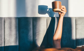 A woman handling a cup of coffee in her bed