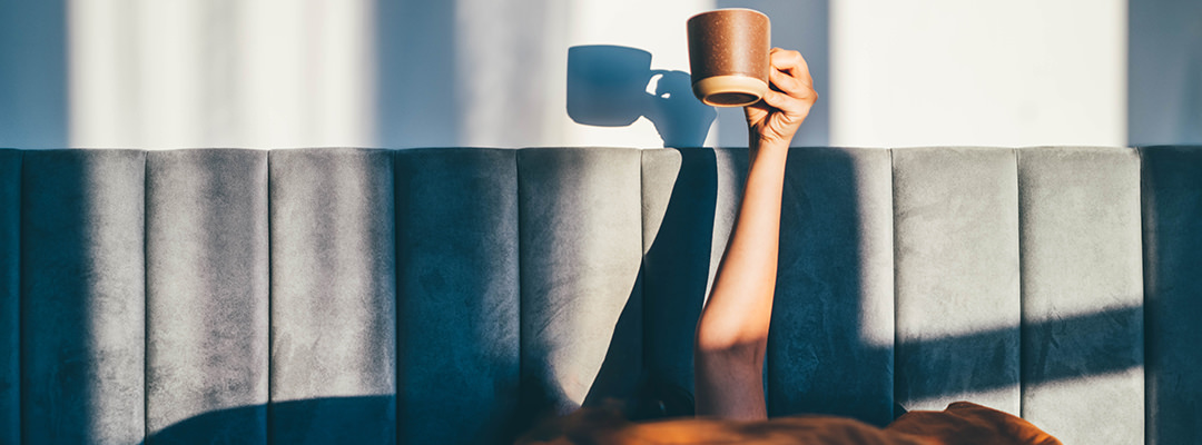 A woman handling a cup of coffee in her bed