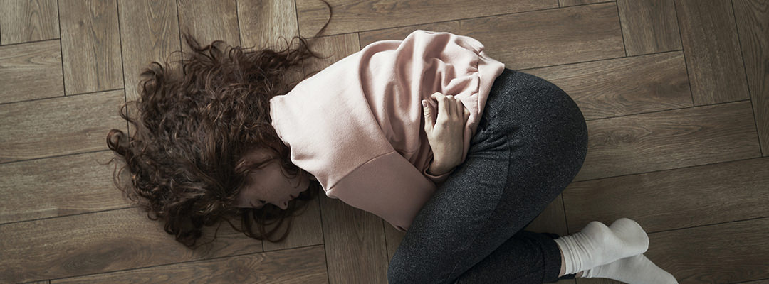 A young woman lying on floor and having strong stomachache
